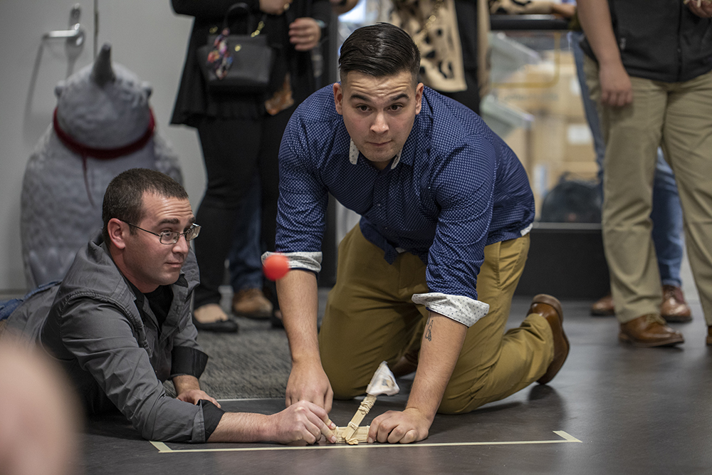 Two team members test their catapult built out of popsicle sticks, dowels, and rubber bands. (Photo Credit: Sean McNeil)