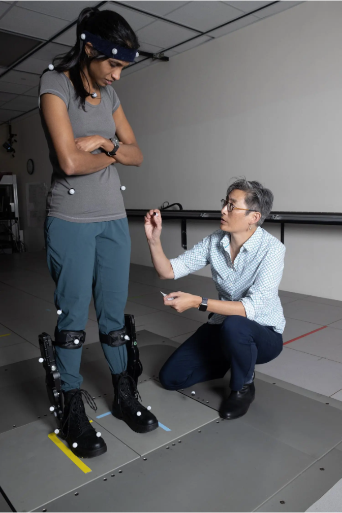 Lena Ting, right, applies motion capture sensors to Surabhi Simha for a standing balance test with robotic ankle exoskeleton boots.
